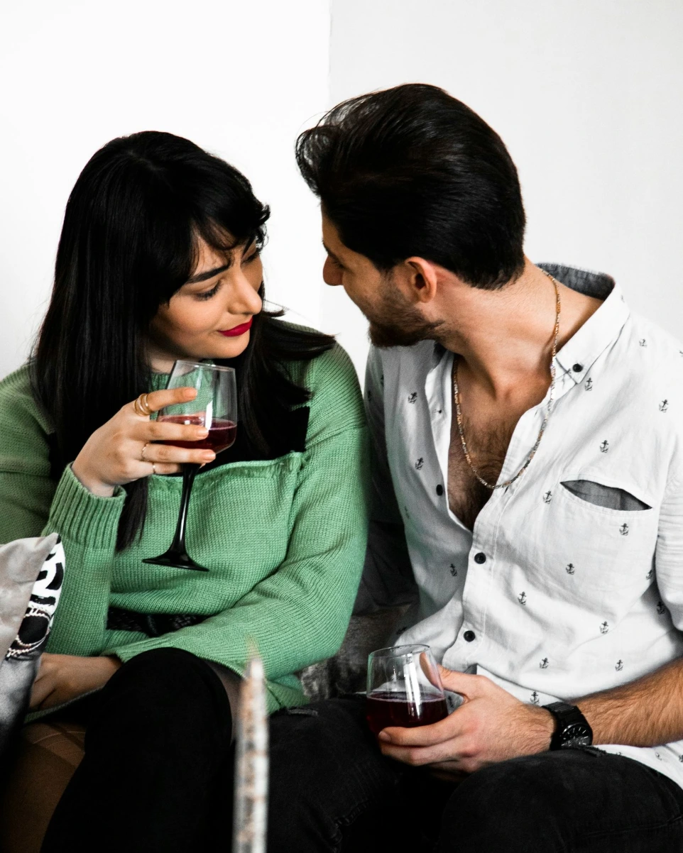 a man and woman sitting next to each other holding wine glasses